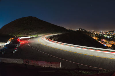 Light trails on mountain road against clear sky at night