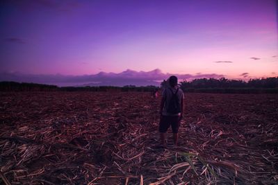 Rear view of woman standing on field against sky during sunset