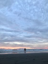 People standing on beach against sky during sunset