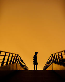 Silhouette man standing by railing against orange sky