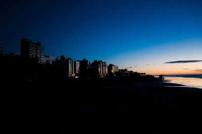 Silhouette buildings at beach against clear sky