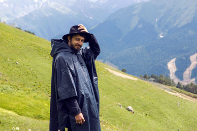 Man with a beard shepherd standing in the mountains in a black raincoat in the rain