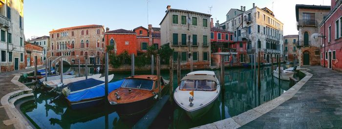 Panoramic shot of boats moored at canal against buildings