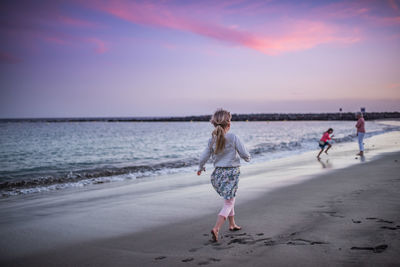 Rear view full length of girl walking at beach during sunset