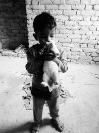 Boy kissing rabbit while standing against brick wall