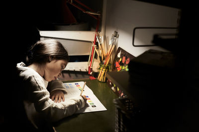 High angle view of girl studying while sitting at illuminated desk in darkroom