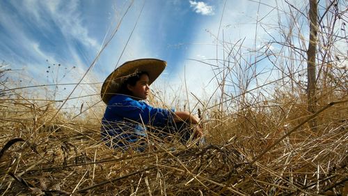 Side view of woman wearing hat sitting on grassy field against sky