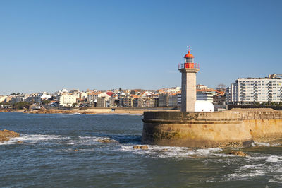Buildings lighthouse by sea against clear blue sky