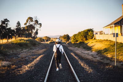 Rear view of woman running on railroad track against clear sky