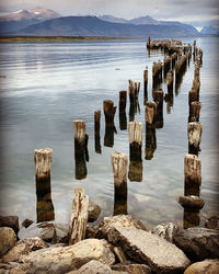 Wooden posts on rocks by sea against sky at puerto natales
