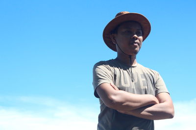 Low angle view of young man standing against blue sky