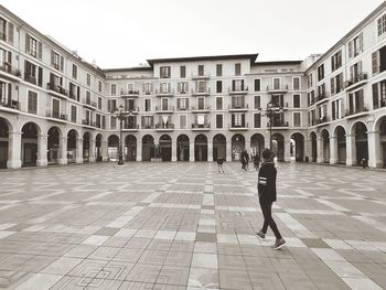 Rear view of woman walking on footpath amidst buildings in city