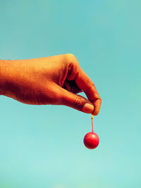Close-up of hand holding strawberry against blue background