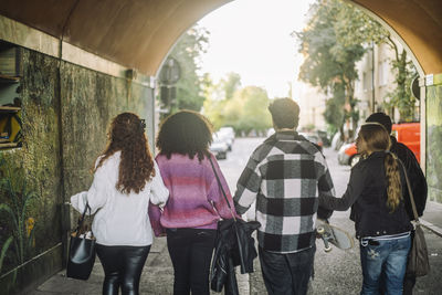 Rear view of male and female friends walking together through underpass