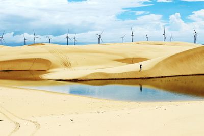 Windmills on sand at beach against cloudy sky