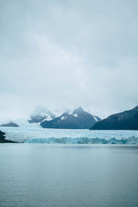 Lake and glacier against snowcapped mountains and cloudy sky