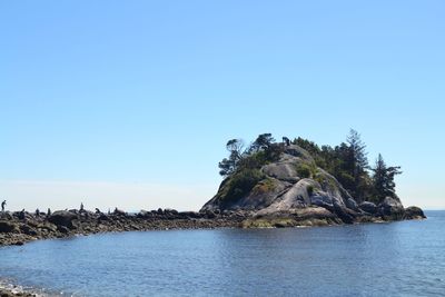 Rock formation in sea against clear blue sky