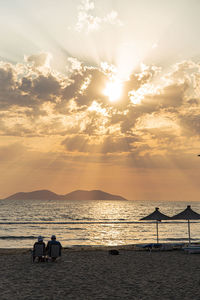 People sitting on beach against sky during sunset