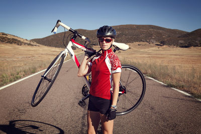 Portrait of confident female cyclist carrying bicycle on country road