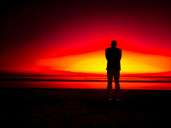 Rear view of silhouette man standing on beach during sunset