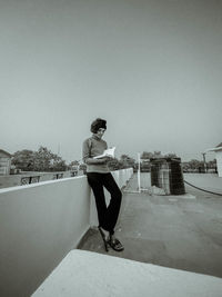 Young man sitting on wall against clear sky