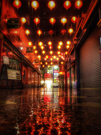 Illuminated lights on wet road amidst buildings at night