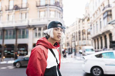 Young man looking away while standing on street in city