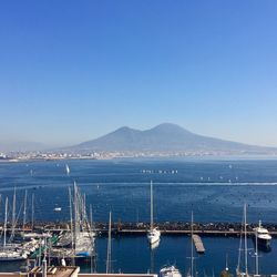 Sailboats moored in sea against clear blue sky