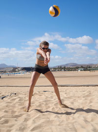 Woman playing volleyball at beach against sky