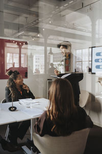 Businessman discussing with female colleagues in meeting at office seen through glass