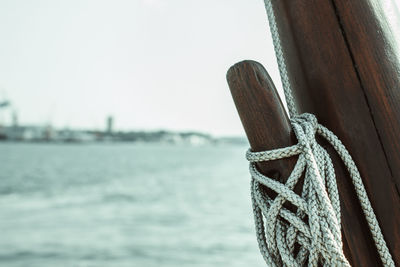 Close-up of rope tied to wooden post in sea against sky