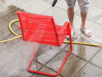 A caucasian guy in gray sweatpants washes a red wire chair