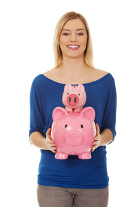 Portrait of smiling young woman holding piggy banks against white background