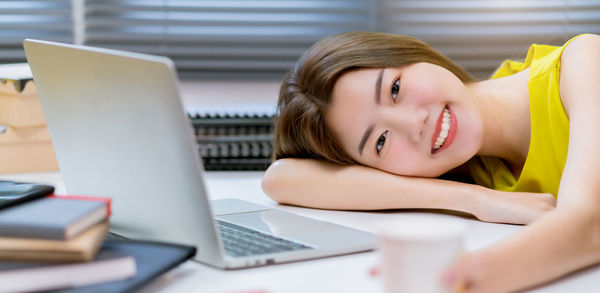 Portrait of young woman using phone while sitting on table