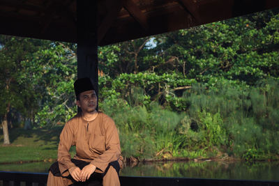 Young man sitting by lake in forest