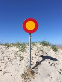 Road sign on sand against clear blue sky