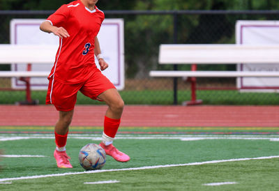 One male soccer player controlling the ball during a match wearing a red uniform.