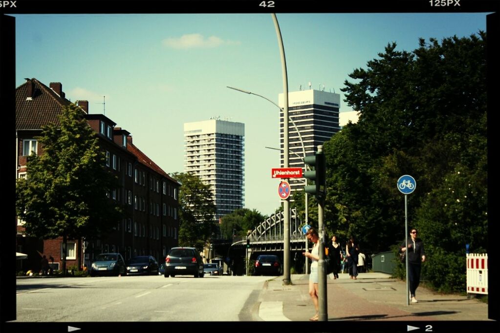 building exterior, architecture, city, built structure, street, transportation, car, road, transfer print, street light, city life, road marking, land vehicle, city street, sky, tree, the way forward, incidental people, skyscraper, mode of transport