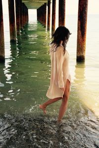 Young woman walking on sea shore below pier