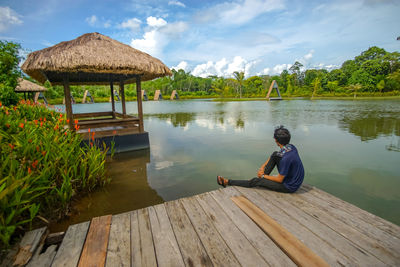 Man sitting on pier over lake against sky