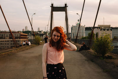 Portrait of smiling redhead woman standing on bridge in city