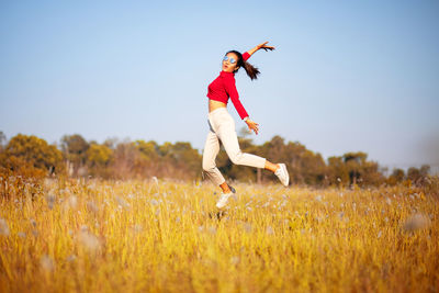 Woman with arms raised jumping on grass against clear sky