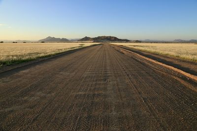 Road amidst field against clear sky