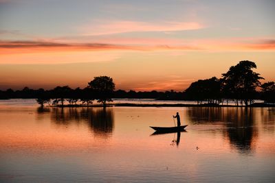 Silhouette man in lake against sky during sunset