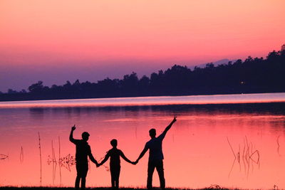 Rear view of silhouette friends standing by river during sunset