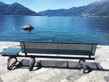 Empty bench by sea against mountains