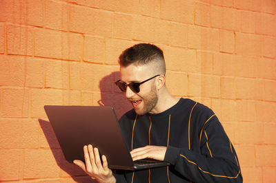 Smiling man using laptop against brick wall
