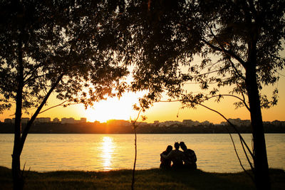 Silhouette people sitting by trees against sky during sunset