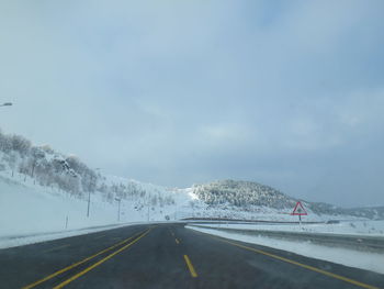 Road by snow covered landscape against sky