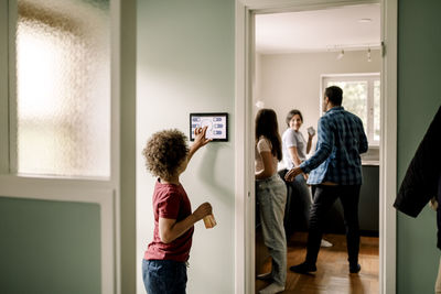 Side view of boy using smart home app on digital tablet while family standing in kitchen